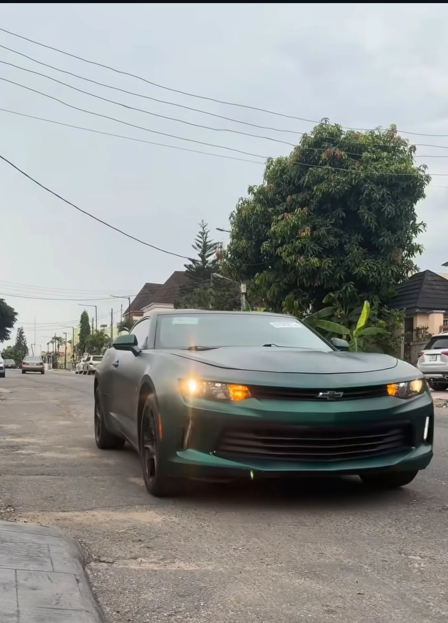 Chevrolet Camaro matte dark green wrap driving Lagos street headlights on front three-quarter view