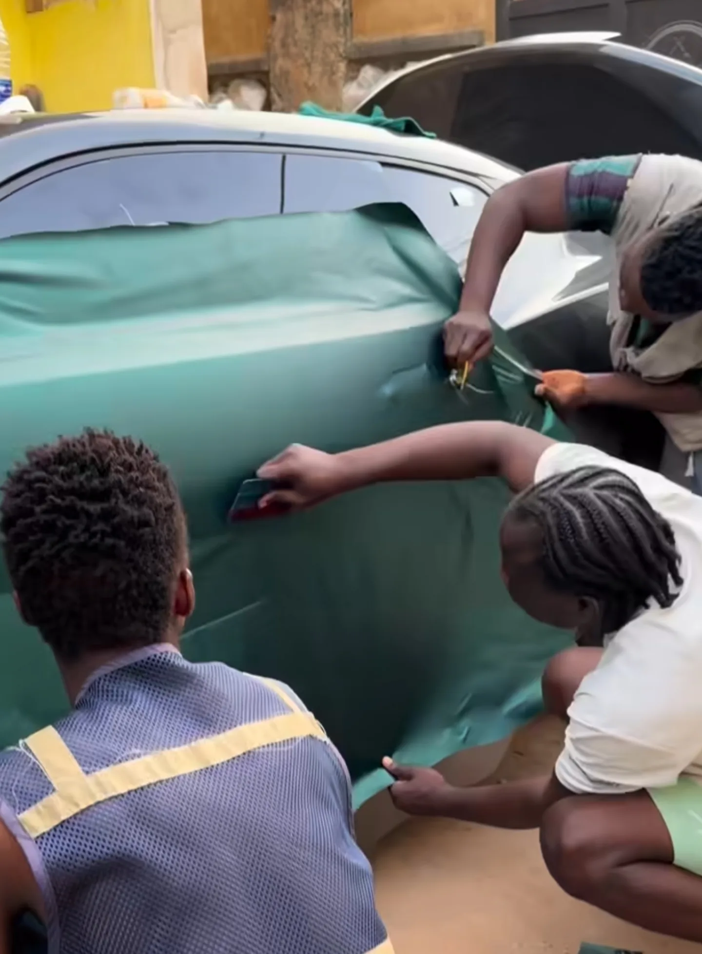 Two technicians wrapping Camaro door panel with dark green vinyl installation Lagos workshop