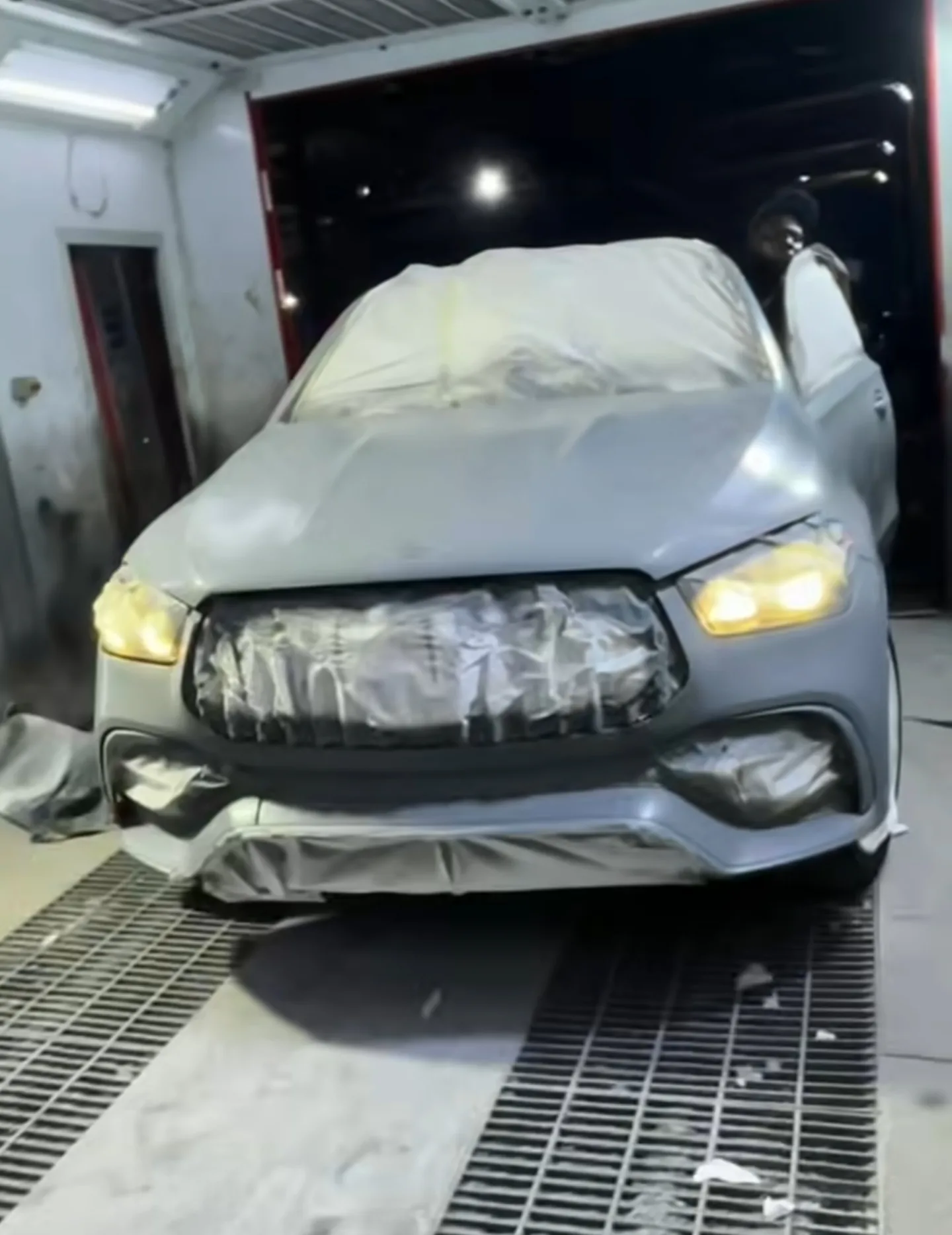 Mercedes GLE 53 in spray paint booth with full masking applied, headlights on during colour change process