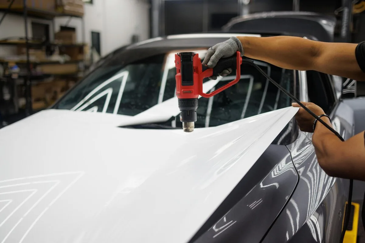 Vinyl wrap technician applying film to car panel with squeegee professional installation